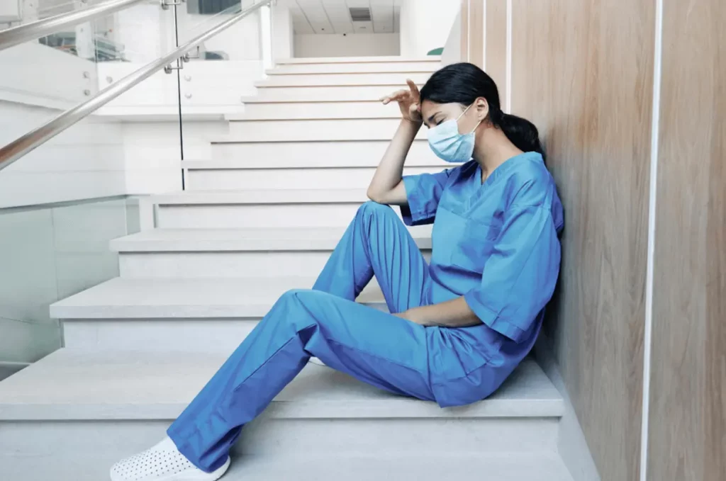 Profesional de la salud agotada, sentada en unas escaleras de un hospital, reflejando el síndrome de burnout